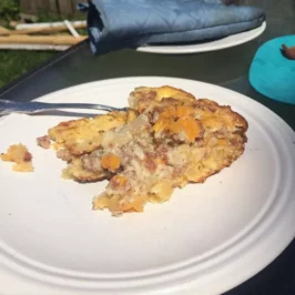 A slice of breakfast bake on a plate. The breakfast bake includes with biscuits, smoked sausage, breakfast potatoes, eggs, and cheese all layered up like a casserole