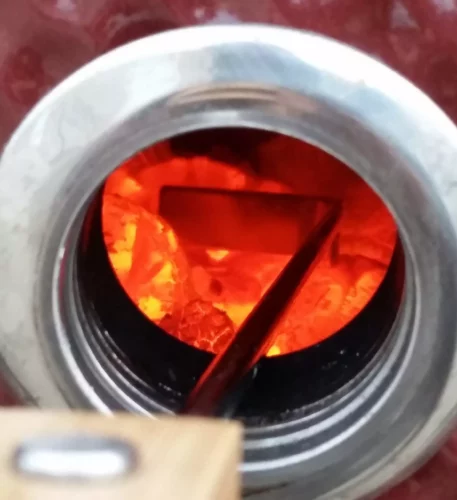 Stocking the hot charcoal with the ash cleaning tool through the smokin chip feeder port, without opening the Saffire