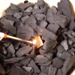 Lighting a grill-safe fire starter square with a long-nosed lighter.