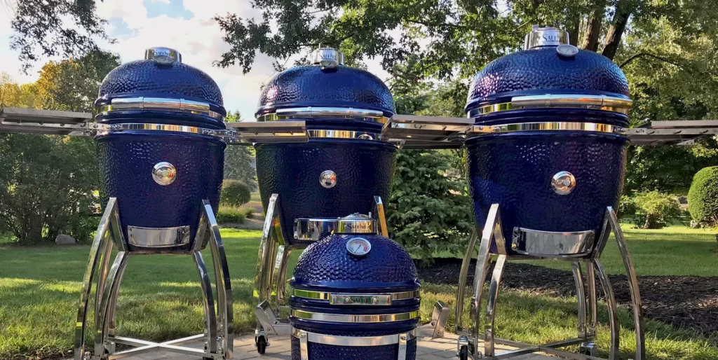 All four sizes of Saffire's blue ceramic smokers standing on a patio with trees and shrubs in the background.