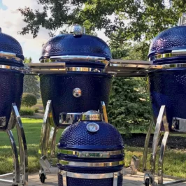 All four sizes of Saffire's blue ceramic smokers standing on a patio with trees and shrubs in the background.