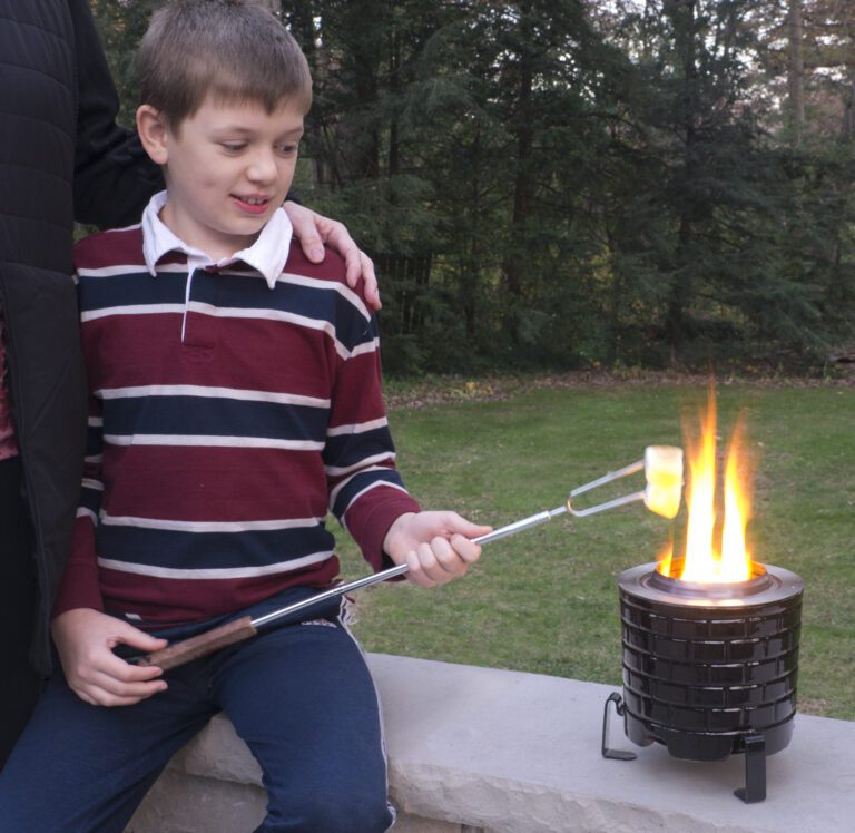 A young boy roasting a marshmallow over a Saffire Tabletop Fire Pit.