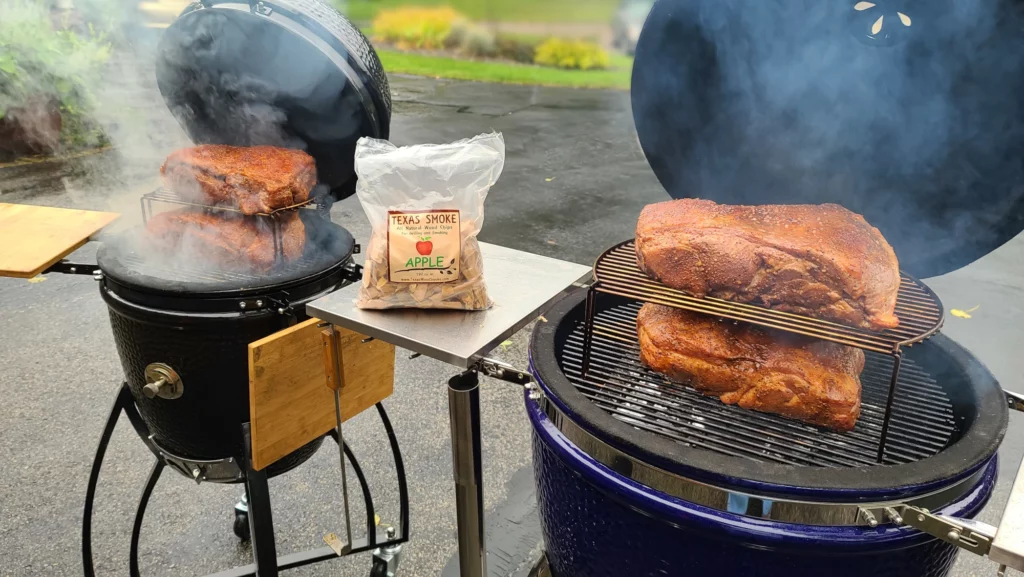 Four pork shoulders are shown being smoked on two Saffire grills. One Saffire is a Medium size grill, and one is a Large size. Both grills have one pork shoulder on the Primary Cooking Grid, and one above that on the elevated Secondary Cooking Grid.