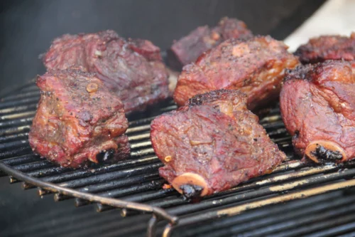 A close-up of shank steak smoking on a kamado grill cooking grid